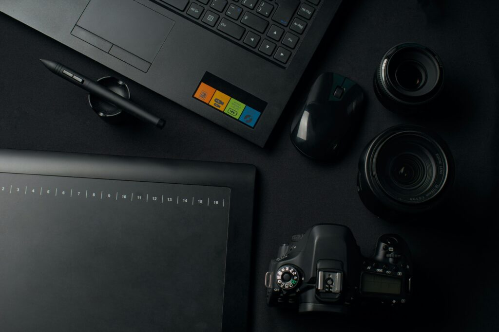 Top view of a modern workspace setup featuring a camera, laptop, graphic tablet, and lenses for photography and editing.